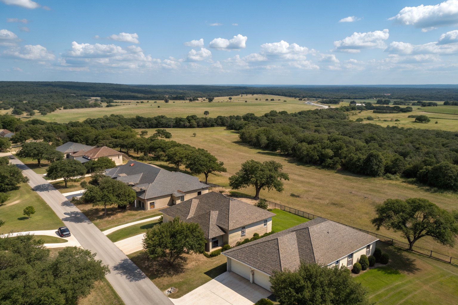 Aerial view of a growing subdivision of shingle-roofed homes among pastures and live oaks