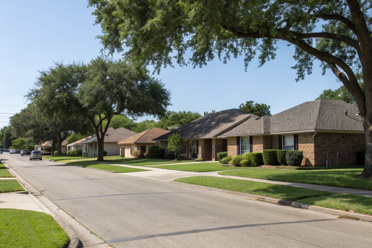 A quiet small-town residential street of brick ranch homes under a big sky