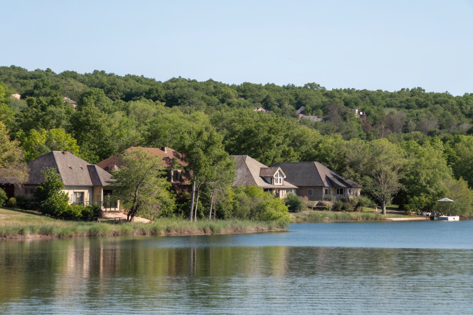 Homes with shingle roofs among trees along the shore of a small lake